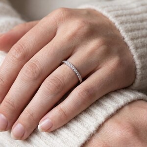 Dainty wedding band worn on finger, featuring a slim half eternity stone row and simple stackable ring style.