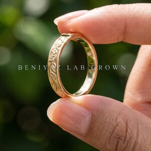 Puede incluir: Un anillo de oro con un intrincado patr&oacute;n floral y de hojas en relieve a lo largo de la banda exterior. El texto BENIYAZ LAB GROWN est&aacute; impreso en el centro de la imagen. El anillo tiene un acabado pulido y una superficie interior lisa.
