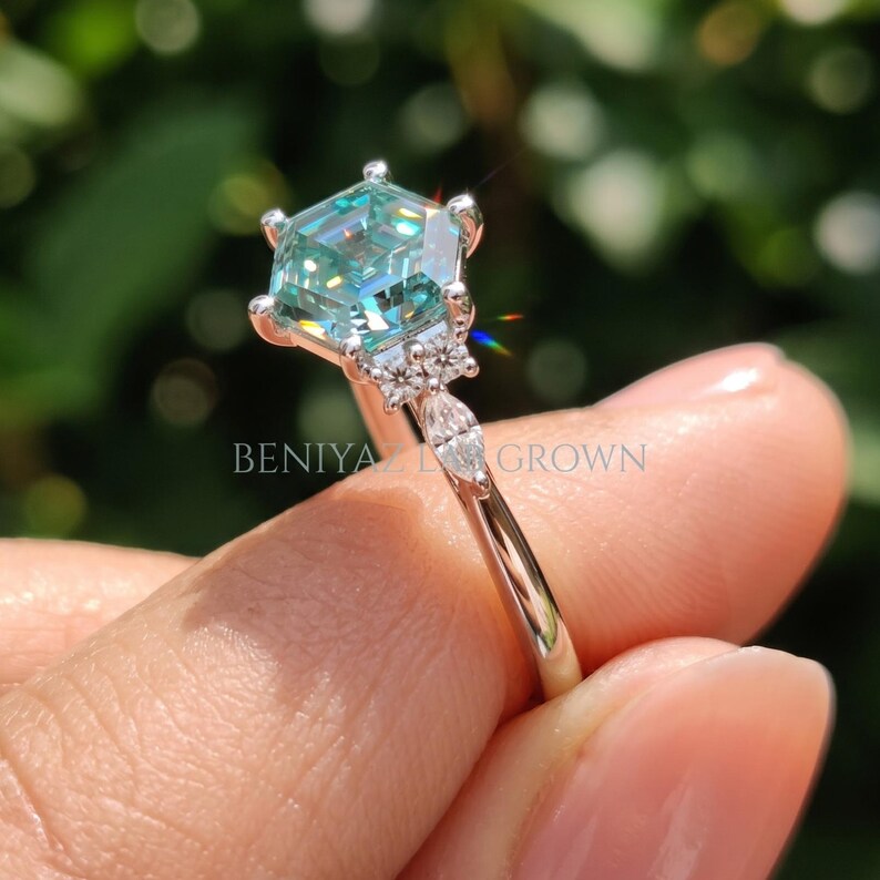 Side profile of cyan blue moissanite ring showing raised prong setting, slim tapered shank and geometric engagement ring structure.