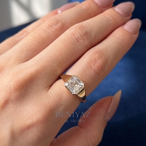 Top-view hand photo featuring a 1.55 CT Asscher cut lab grown diamond ring in 14K yellow gold. The bezel set signet engagement ring is worn on the ring finger and displays an IGI certified D color VVS1 lab grown diamond, combining a modern statement ring look with a clean luxury aesthetic.