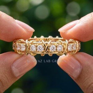 Hand-held close-up of a lab grown diamond eternity wedding band showing round brilliant diamonds and polished criss-cross crossover details.