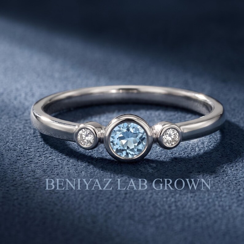 Three stone blue gemstone ring with two bezel set natural diamond accents on a slim polished yellow gold band.