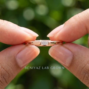 Hand held baguette lab grown diamond solitaire band showing the east west stone and delicate 1.5mm gold shank.