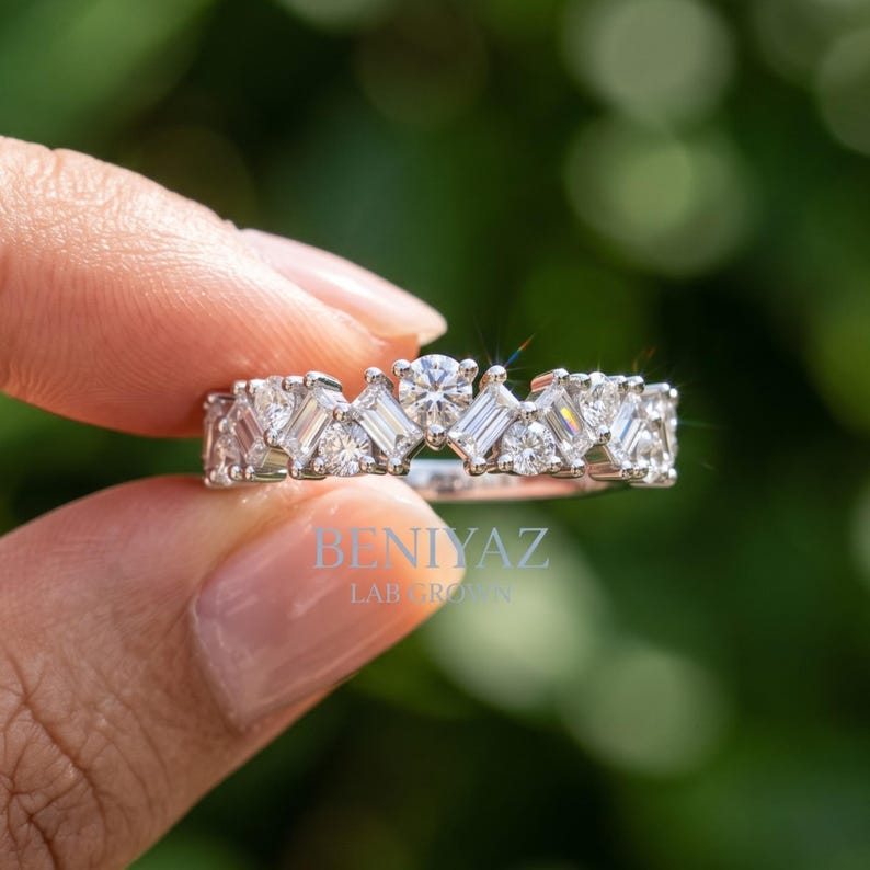 May include: A silver-toned ring featuring a band set with alternating round and baguette-cut clear stones. The text BENIYAZ LAB GROWN is printed in light blue on the center of the band. The design showcases a repeating pattern of faceted gems.