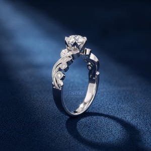 Front view of a white gold lab grown diamond engagement ring with a round brilliant center diamond, vintage leaf pattern, milgrain edges and small diamond accents along the band.