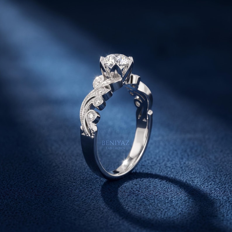 Front view of a white gold lab grown diamond engagement ring with a round brilliant center diamond, vintage leaf pattern, milgrain edges and small diamond accents along the band.