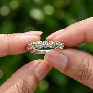 Detailed view of a round peridot gemstone ring with sculpted leaf accents and open botanical shank.