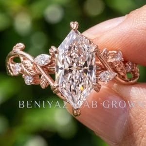 Hand displaying a marquise lab grown diamond engagement ring in rose gold with branch style setting and delicate woodland vine details against green foliage
