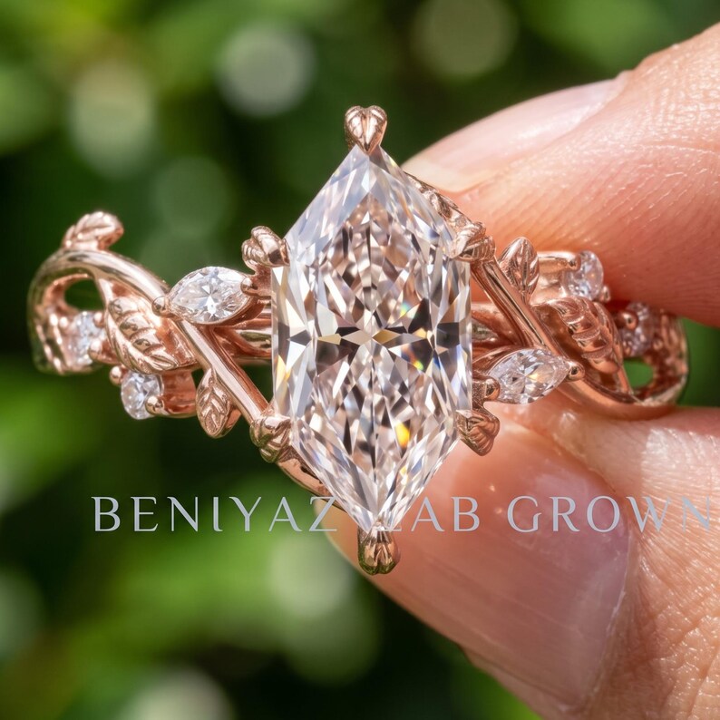 Hand displaying a marquise lab grown diamond engagement ring in rose gold with branch style setting and delicate woodland vine details against green foliage