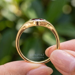 Close up of kite set red stone ring with a single burgundy gemstone, smooth flush setting and polished signet style band.