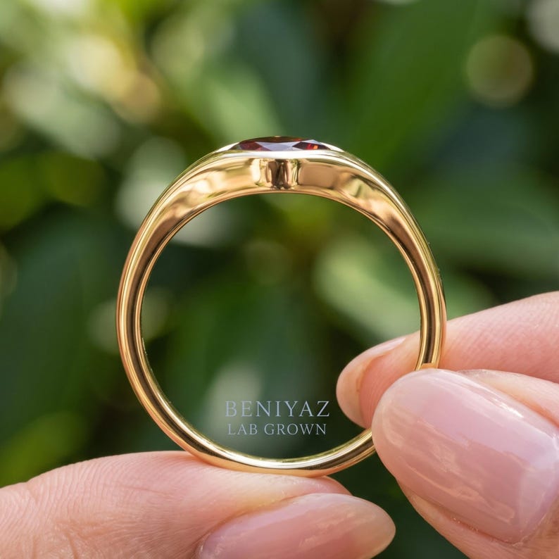 Close up of kite set red stone ring with a single burgundy gemstone, smooth flush setting and polished signet style band.