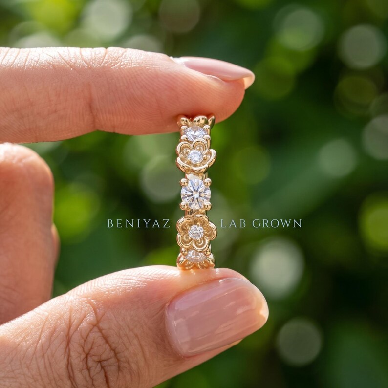 May include: A gold ring featuring a repeating floral pattern with alternating round brilliant cut diamonds set within the petals. The band displays the text BENIYAZ LAB GROWN in white lettering across the center of the ring design.