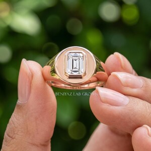 Hand held rose gold emerald cut diamond signet ring showing the vertical rectangular center stone and polished face.