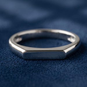 Custom engravable bar signet ring held between fingers, showing the slim band and rectangular flat top face.