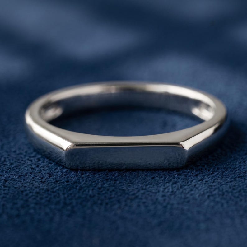 Custom engravable bar signet ring held between fingers, showing the slim band and rectangular flat top face.