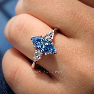 Blue marquise lab grown diamond engagement ring worn on hand, showing the scale of the elongated center stone and three stone design.