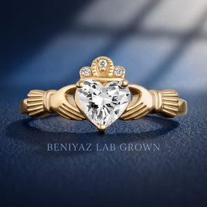 Front hand held view of a heart cut diamond Claddagh promise ring with traditional hands, heart and crown symbolism.