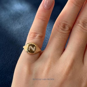 Hand holding a custom yellow gold initial N diamond signet ring, displaying the polished side profile, ring thickness and premium personalized signet design.