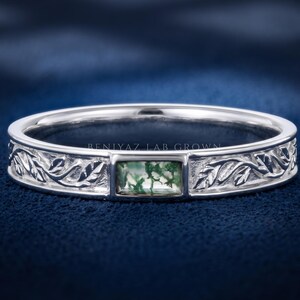 Puede incluir: Un anillo de tono plateado con una piedra preciosa rectangular de &aacute;gata musgosa en el centro. La banda est&aacute; decorada con un patr&oacute;n de hojas en relieve a ambos lados de la piedra. El texto BENIYAZ LAB GROWN es visible en la superficie interior.