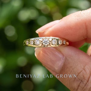 Starburst lab grown diamond band held between fingers showing seven round diamonds in engraved celestial star settings