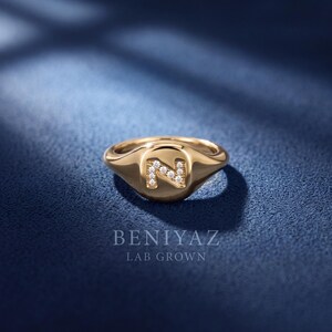 Personalized letter N signet ring crafted in 14K yellow gold with lab grown diamond accents, shown from a front three-quarter angle on a dark blue luxury background.