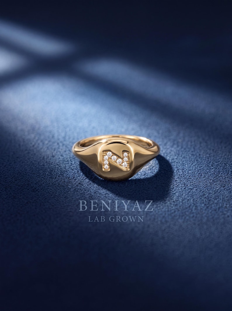 Personalized letter N signet ring crafted in 14K yellow gold with lab grown diamond accents, shown from a front three-quarter angle on a dark blue luxury background.