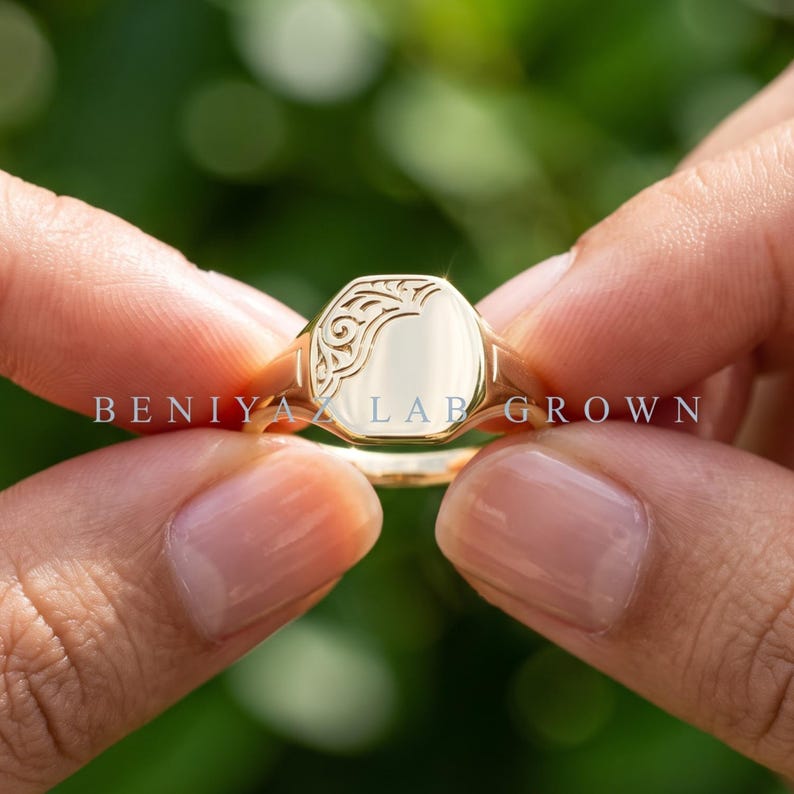 Custom oval signet ring held by hand showing smooth high polish face, ornate floral scrollwork detail and tapered band