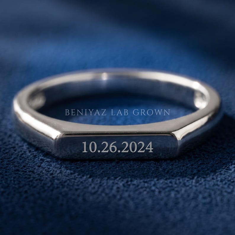 Custom engravable flat top signet ring held between fingers, showing the clean rectangular face and polished finish.