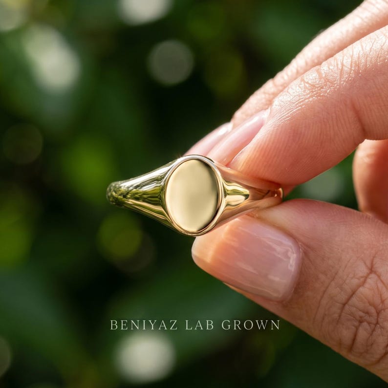 Close up small oval signet ring held by hand showing blank oval face, high polish finish and delicate tapered shoulders