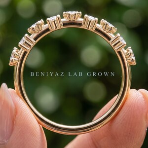 May include: A gold band ring featuring a series of round, clear stones set in individual prongs along the top half of the band. The text BENIYAZ LAB GROWN is printed in white across the center of the ring. The band has a smooth, polished finish.