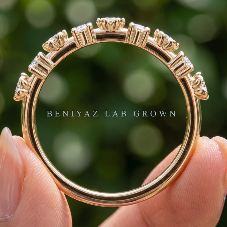 May include: A gold band ring featuring a series of round, clear stones set in individual prongs along the top half of the band. The text BENIYAZ LAB GROWN is printed in white across the center of the ring. The band has a smooth, polished finish.