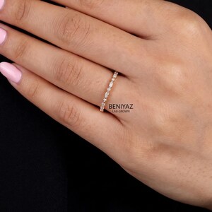 A woman's hand with soft pink manicured nails displaying a dainty diamond wedding band against a dark background. The ring features horizontally arranged marquise cut lab grown diamonds accented by small round stones. Its slim white-tone band creates a refined, minimalist appearance, ideal for wearing alone or alongside an engagement ring.