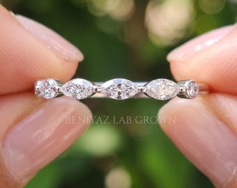 Puede incluir: Un anillo de banda plateada con una hilera de piedras transparentes alternadas en corte marquesa y redondo. El texto BENIYAZ LAB GROWN está impreso en blanco en la parte inferior de la imagen. El anillo se sostiene horizontalmente sobre un fondo verde borroso.