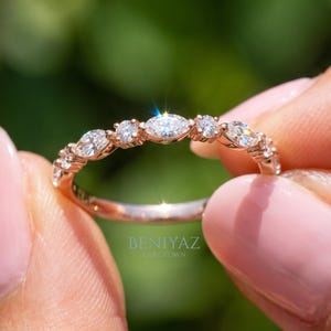 Close up of thin rose gold marquise and round diamond stacking ring held between fingertips