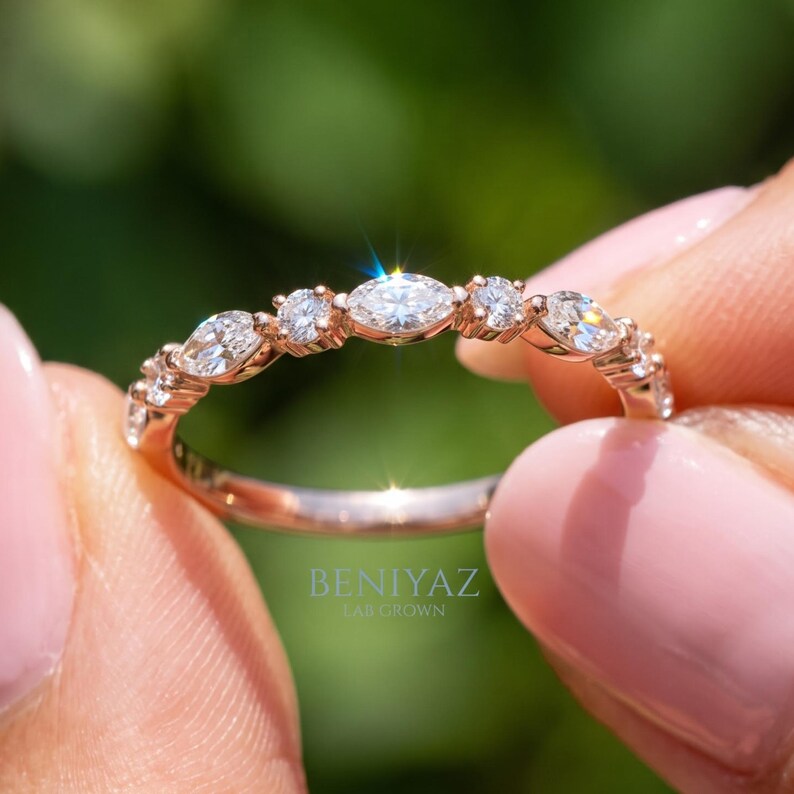 Close up of thin rose gold marquise and round diamond stacking ring held between fingertips