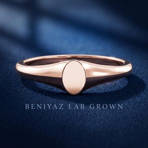 Front view of petite oval signet ring on blue background with plain polished face and slim tapered half round band