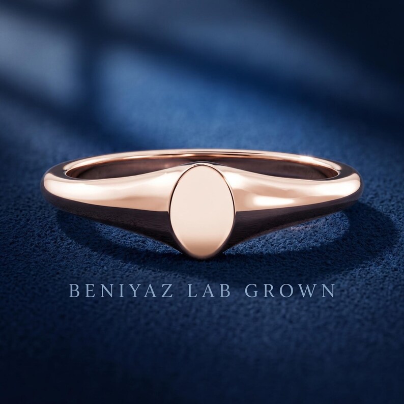 Front view of petite oval signet ring on blue background with plain polished face and slim tapered half round band