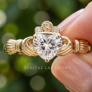 Angled studio view of a yellow gold Claddagh ring showing the heart shaped center diamond, crown and sculpted hands from the side.