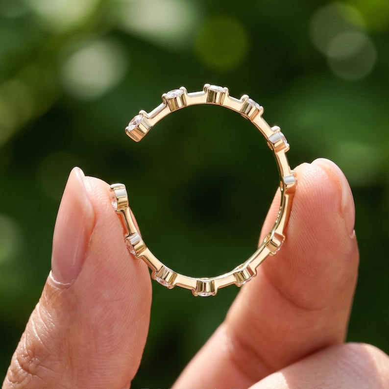 Hand displaying an open band lab grown diamond ring in yellow gold with sparkling round diamond ends, photographed against soft green foliage
