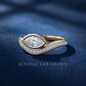 Marquise bezel set diamond engagement ring with matching contour wedding band, two tone gold design shown from a three-quarter angle on dark blue background.