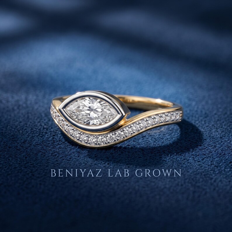 Marquise bezel set diamond engagement ring with matching contour wedding band, two tone gold design shown from a three-quarter angle on dark blue background.