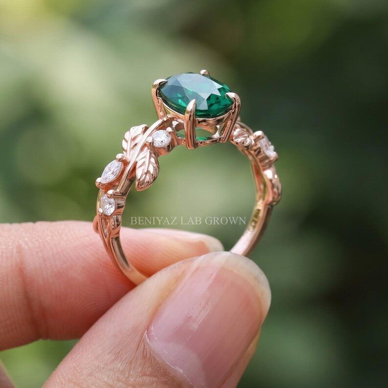 Green stone engagement ring shown at an angle with oval emerald center, sculpted leaves and nature inspired details.