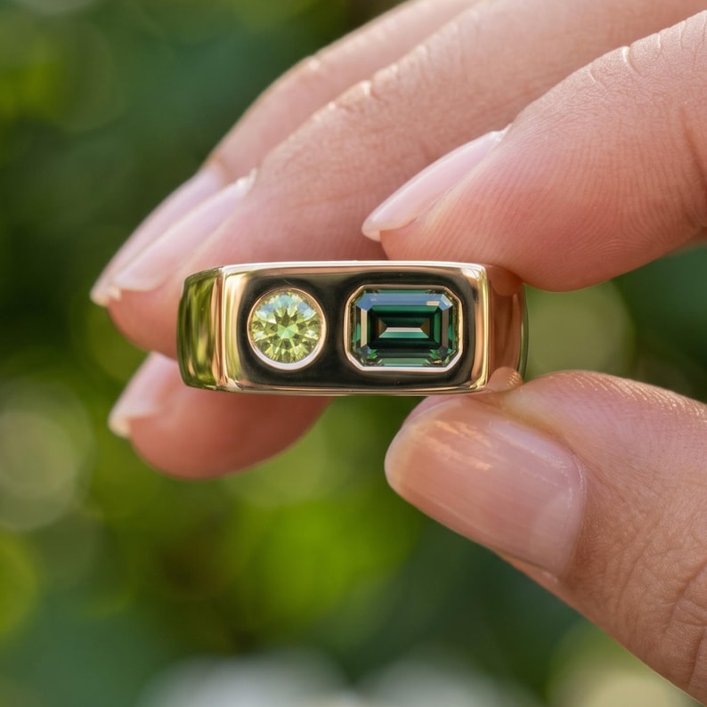 Detailed hand view of a modern sapphire signet ring featuring an emerald cut teal sapphire and smaller round green sapphire in an asymmetrical design