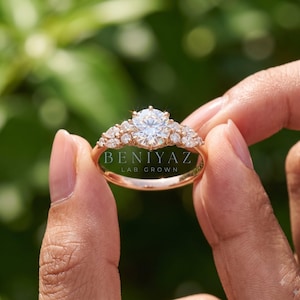 Hand holding a delicate round lab grown diamond ring by the band, highlighting the slim solid gold setting and fine minimalist engagement ring design