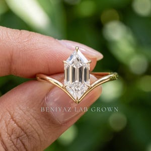 Close up outdoor view of a Dutch Marquise diamond engagement ring held between fingers with a minimalist V-shaped band.