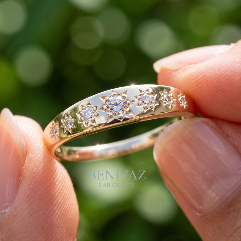 Angled close up of seven stone lab grown diamond band showing engraved starburst settings and polished tapered gold ring