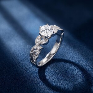 Side profile of a white gold round lab grown diamond engagement ring highlighting the raised center setting, vintage leaf motif and detailed diamond accented shoulders.