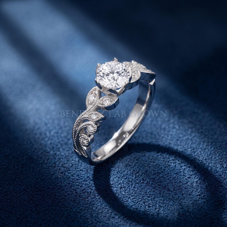Side profile of a white gold round lab grown diamond engagement ring highlighting the raised center setting, vintage leaf motif and detailed diamond accented shoulders.