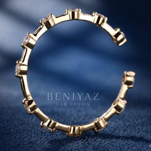 May include: A gold open-style ring featuring a series of evenly spaced, round, clear stones set along the band. The text BENIYAZ LAB GROWN is visible in the center of the ring. The band has a polished finish and a circular, incomplete design.