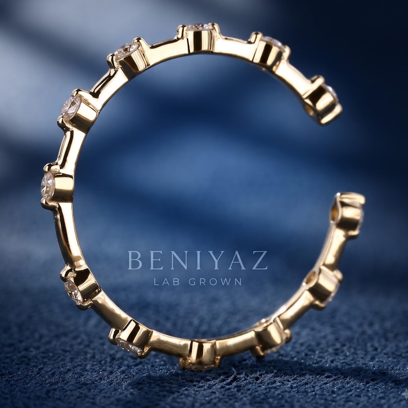 May include: A gold open-style ring featuring a series of evenly spaced, round, clear stones set along the band. The text BENIYAZ LAB GROWN is visible in the center of the ring. The band has a polished finish and a circular, incomplete design.
